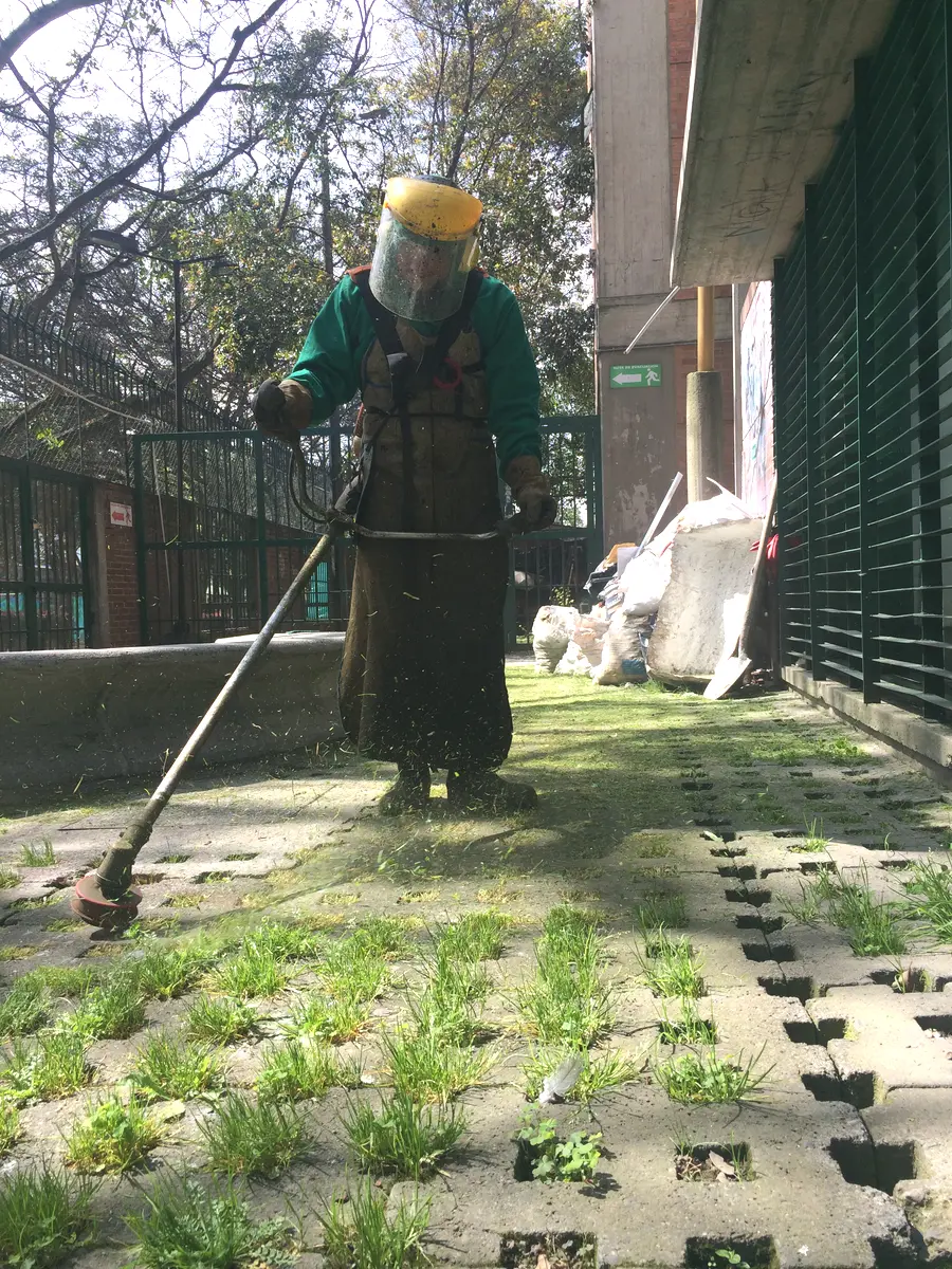 Operario con protección facial realizando rocería de detalle entre superficies permeables